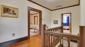 A spacious room with hardwood floors, a wooden staircase, and a bed with a floral bedspread.