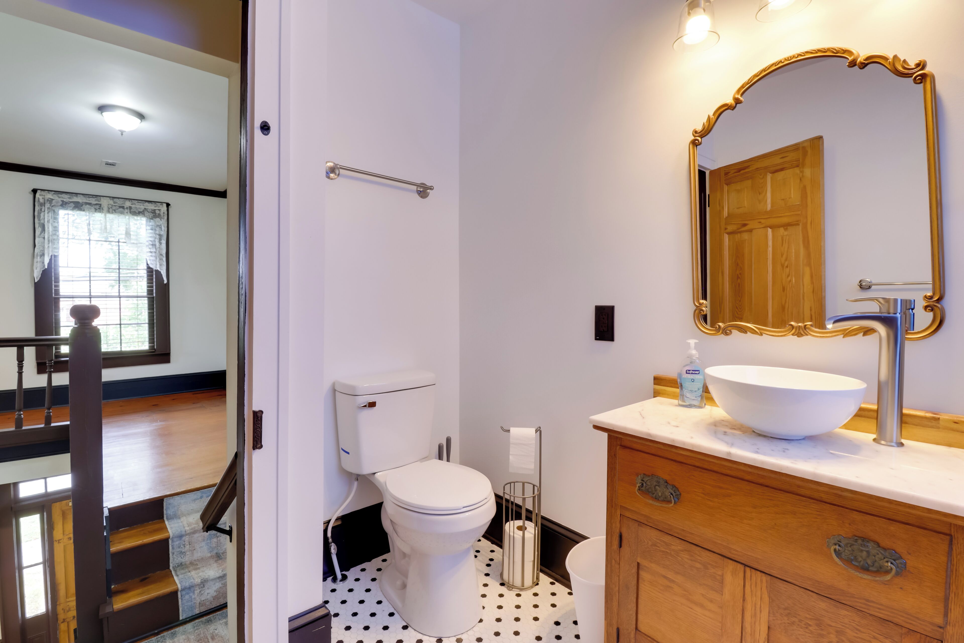 A bathroom with a white toilet, a wooden vanity with a large mirror, and a white sink.