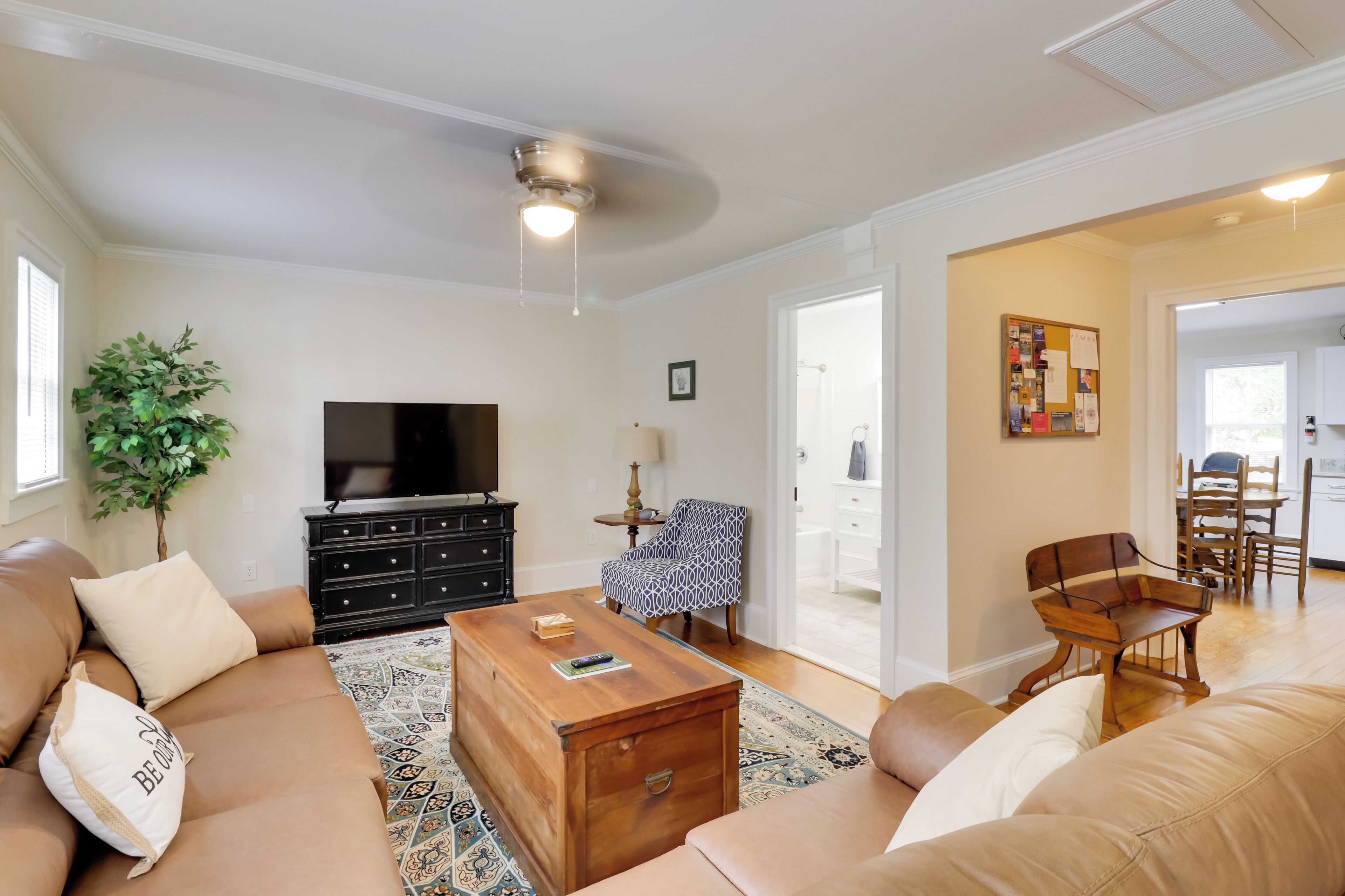 A living room with a sofa, a coffee table, a TV, a plant, and a dining area with chairs and a table.