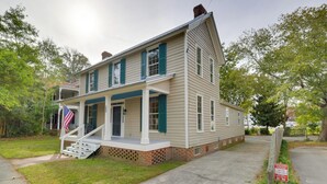 A two-story house with a front porch, a brick foundation, and a flag.