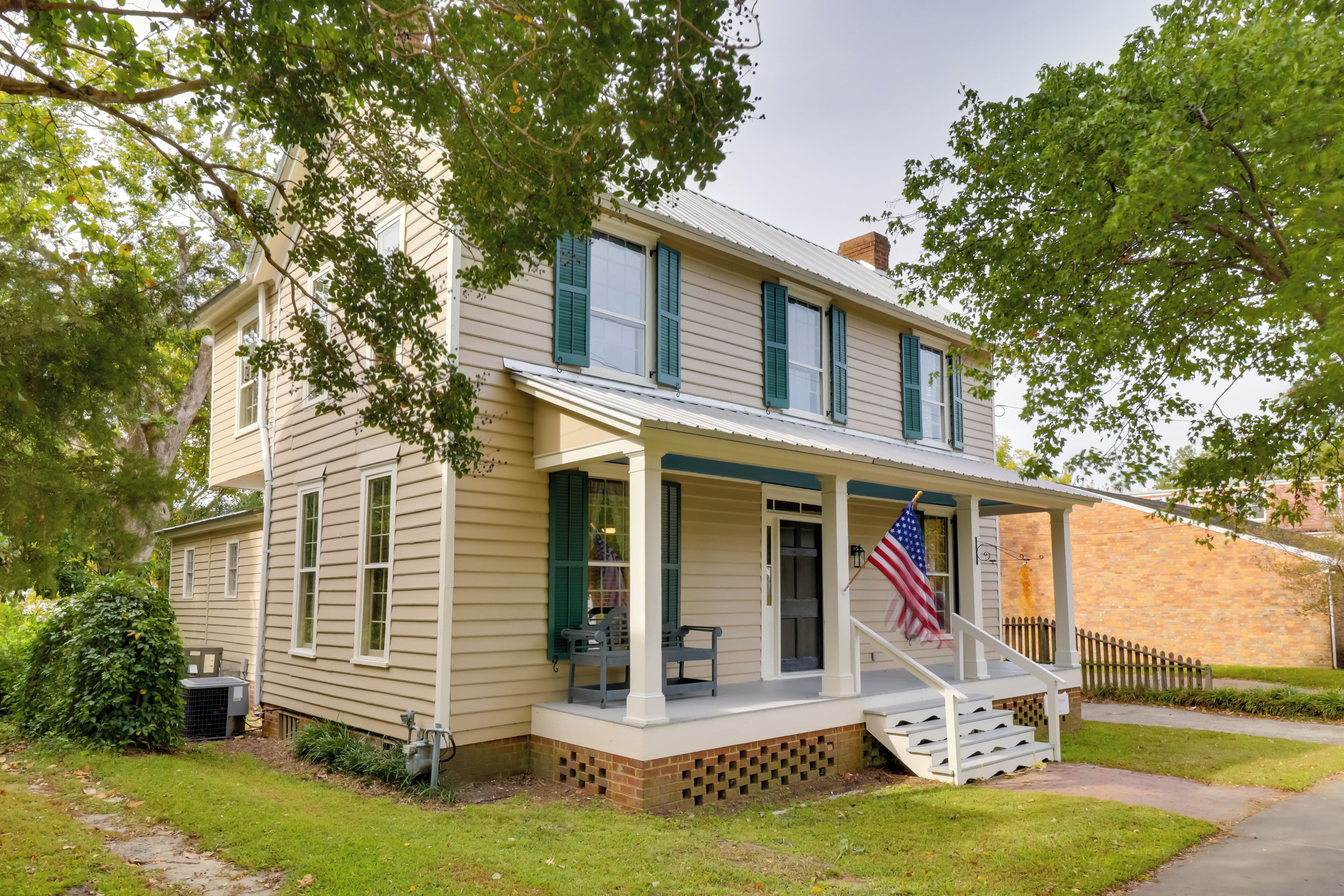 A two-story house with a porch, a brick foundation, and an American flag.