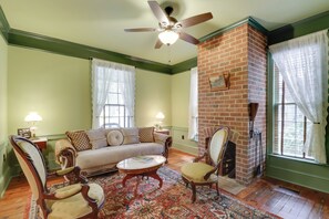 A living room with a brick fireplace, green walls, a ceiling fan, a sofa, two armchairs, and a coffee table. - Walk to Downtown: Family Gem in Historic Edenton (Edenton)