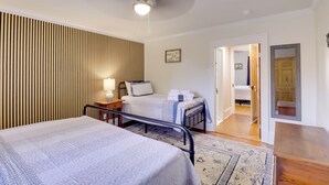 A hotel room with two beds, a ceiling fan, a nightstand, a lamp, and a wooden panel wall.