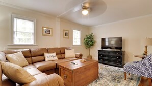 A living room with a brown leather sectional sofa, a wooden coffee table, a black TV stand, and a patterned rug.