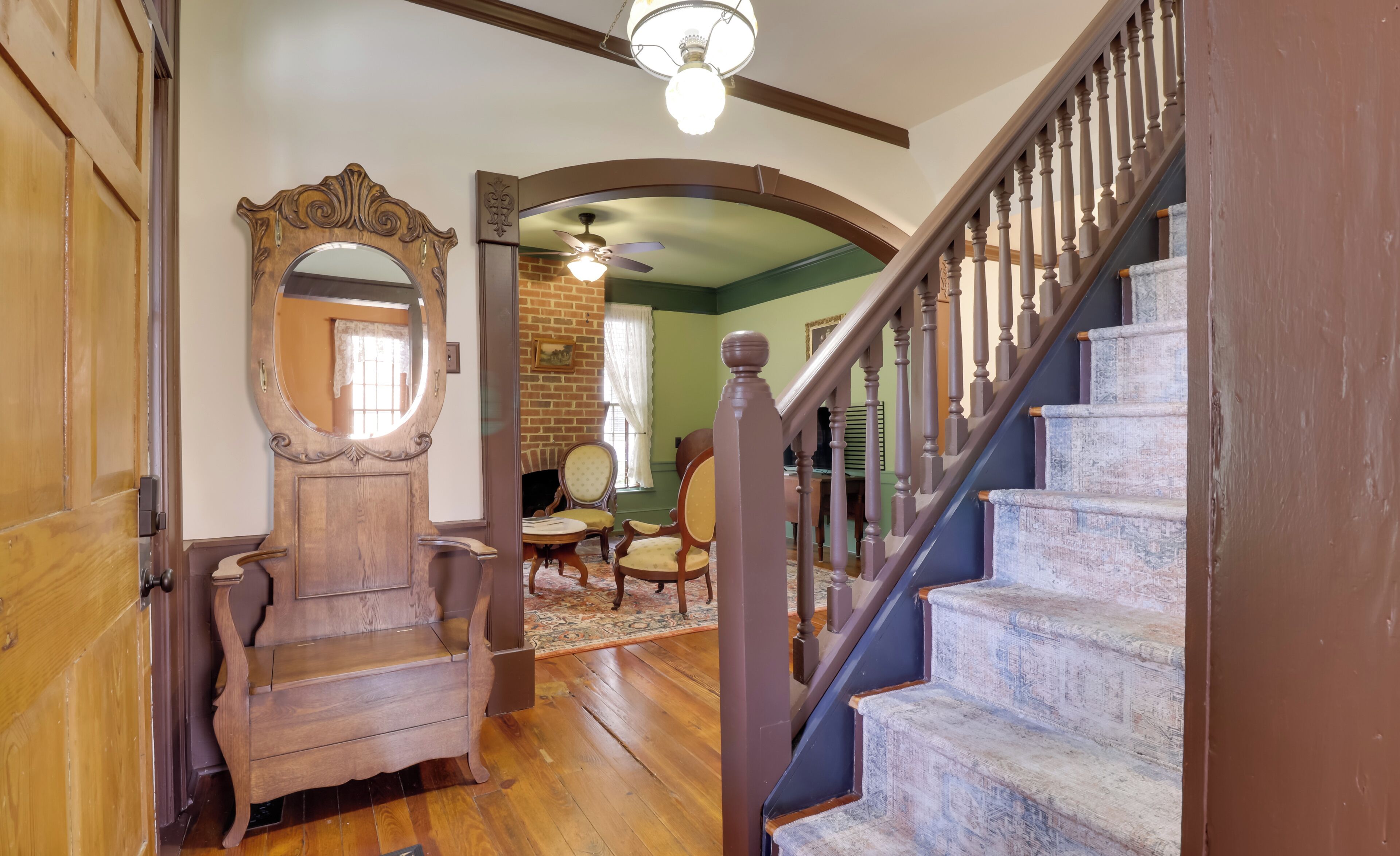 A wooden staircase with a handrail, a round mirror, and a wooden bench in a room with a brick wall and a ceiling fan.
