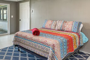 Ein Schlafzimmer mit einem Bett, einer gemusterten Bettdecke, einer aufgerollten Decke und einem blauen Teppich.
