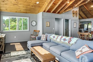 A modern living room with a sectional sofa, a wooden bench, and a dining area with chairs. - Lakefront Family Getaway on Willsboro Point! (Willsboro)