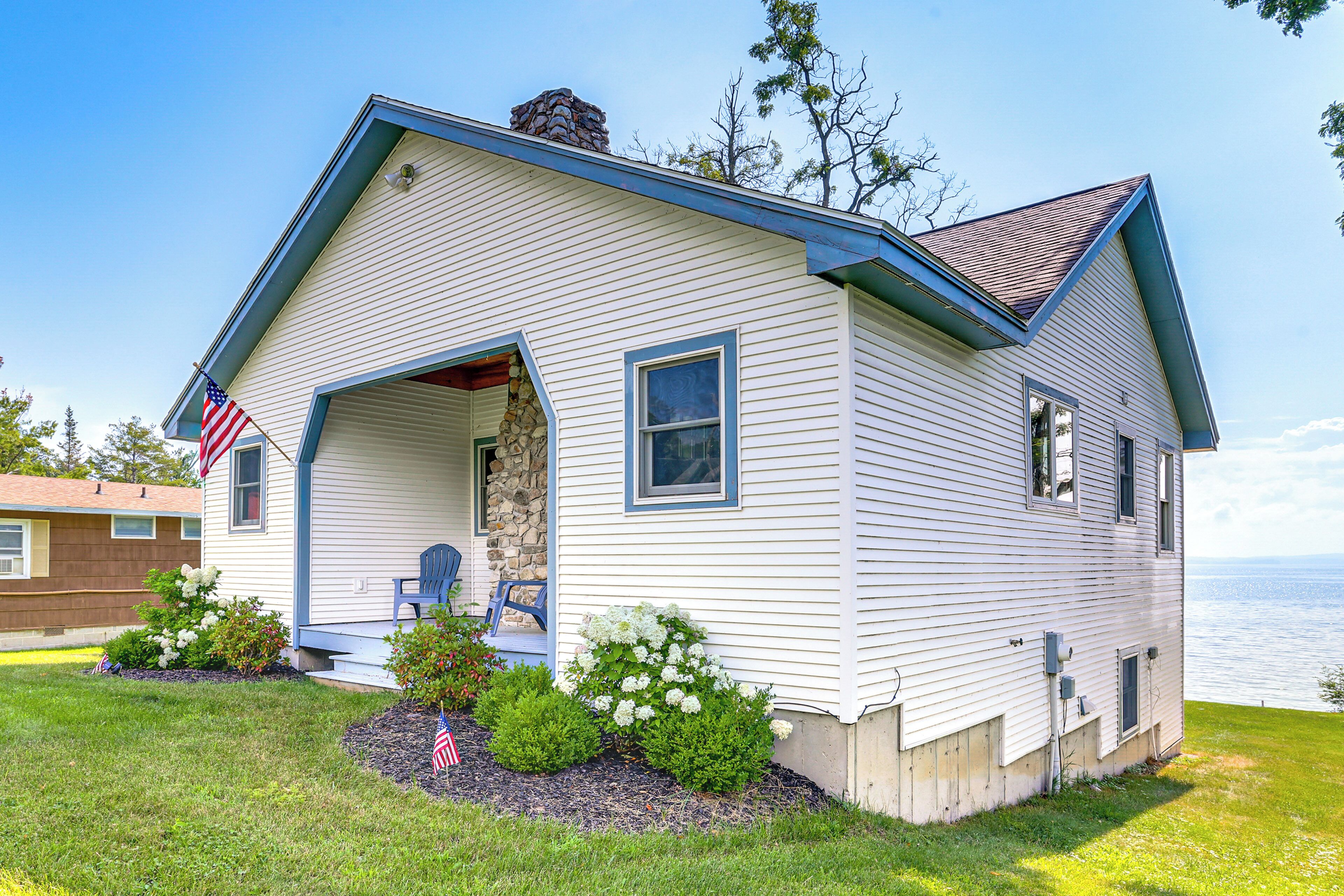 A single-story house with a gabled roof, a stone chimney, and a front porch with two chairs.