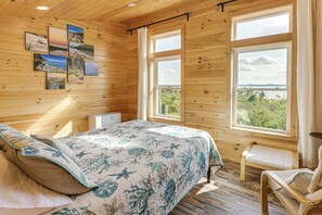 A wooden cabin bedroom with a bed, a chair, and a window with a view. - Path to Private Beach! Couple's Retreat in Cutler (Cutler)