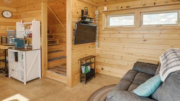 L’intérieur chaleureux d’un chalet comprend un coin cuisine, un espace salon avec un canapé, un téléviseur fixé au mur et un escalier en bois.