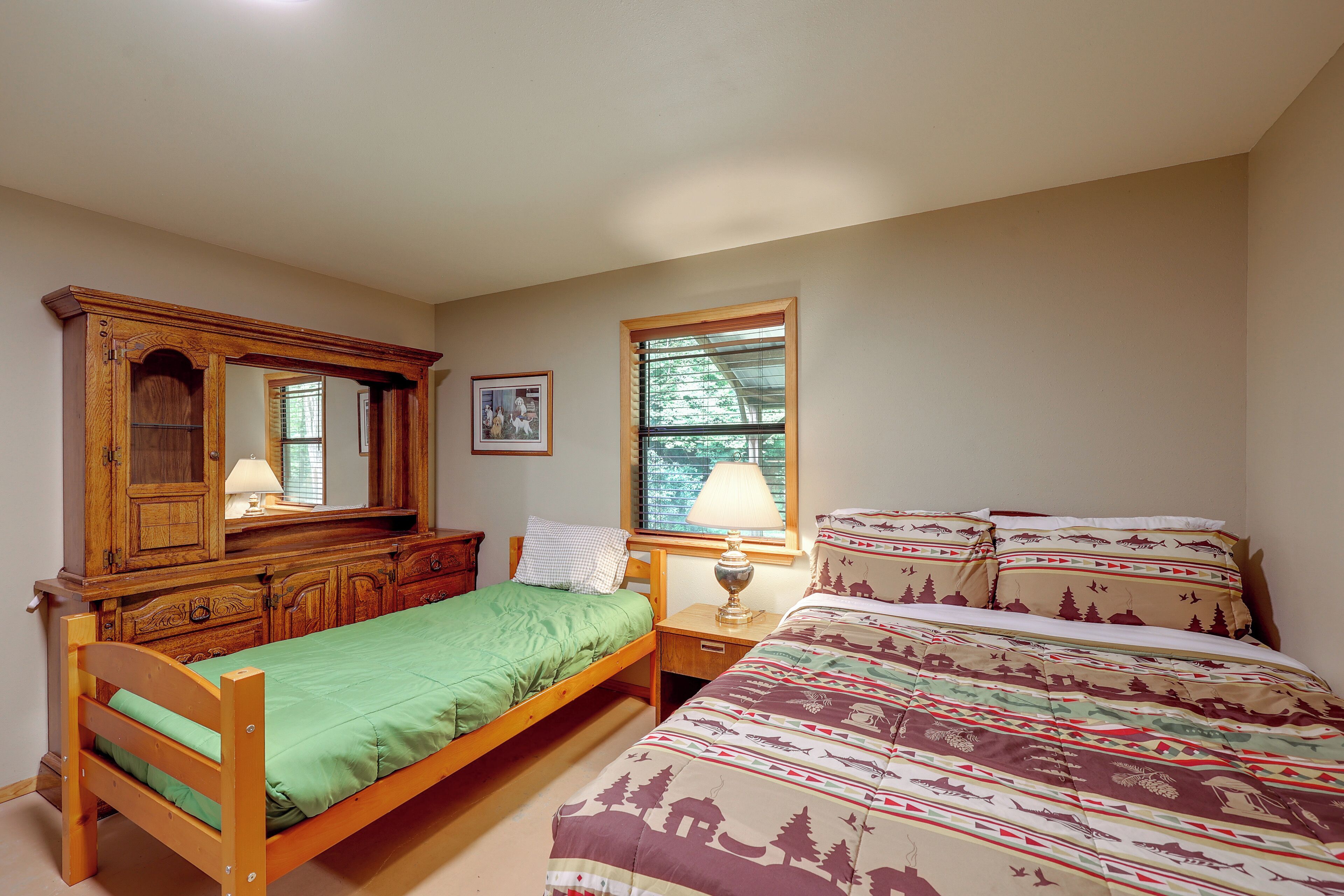A bedroom with a wooden bed, a nightstand, a dresser, a window, and a lamp.