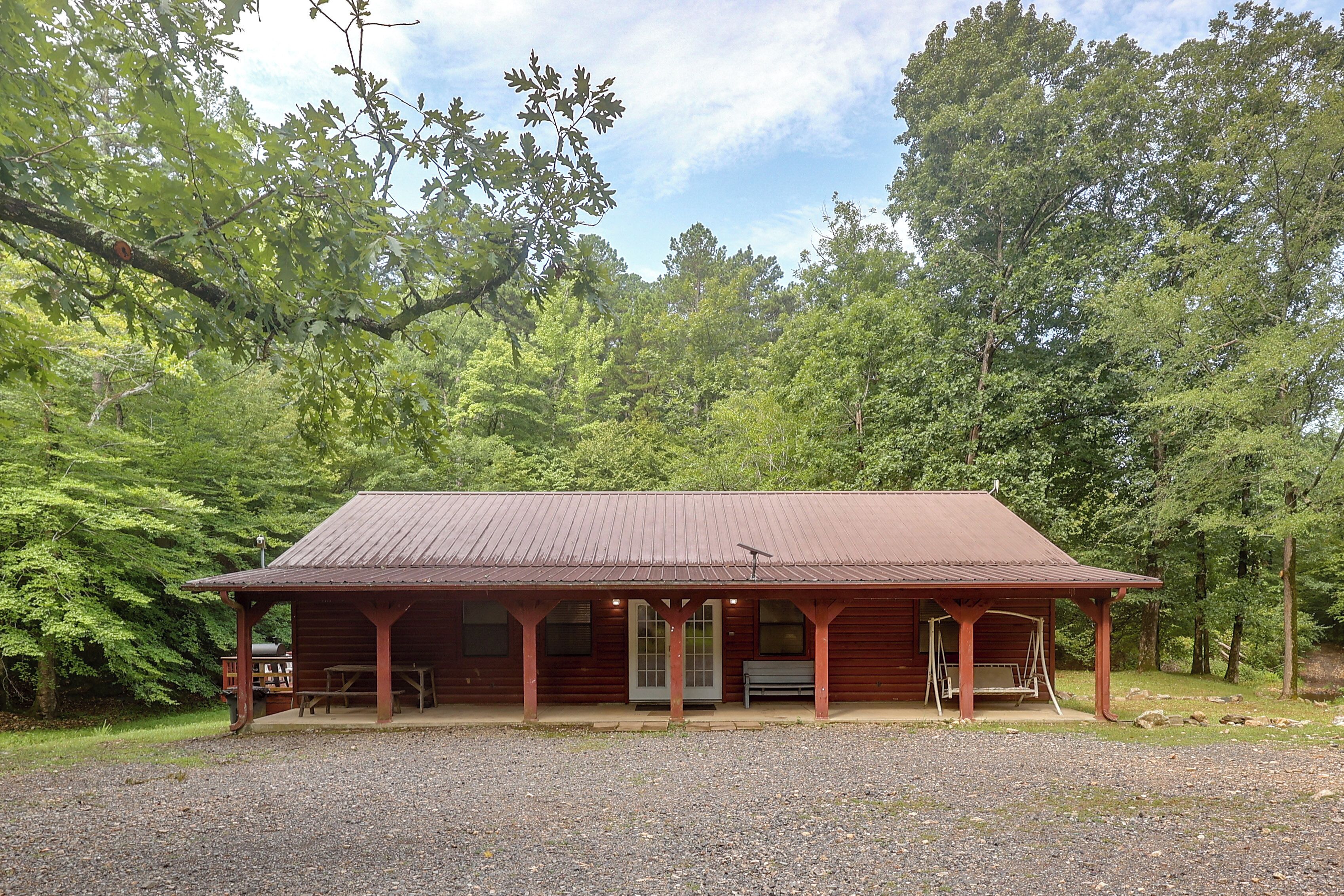 A wooden cabin with a porch, set in a forested area.