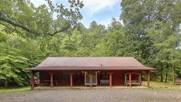 A wooden cabin with a porch, set in a forested area.