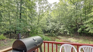 A barbecue grill on a deck overlooking a forested area with a river.
