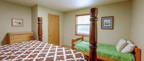 A bedroom with a four-poster bed, a single bed, a dresser, and a window with blinds.