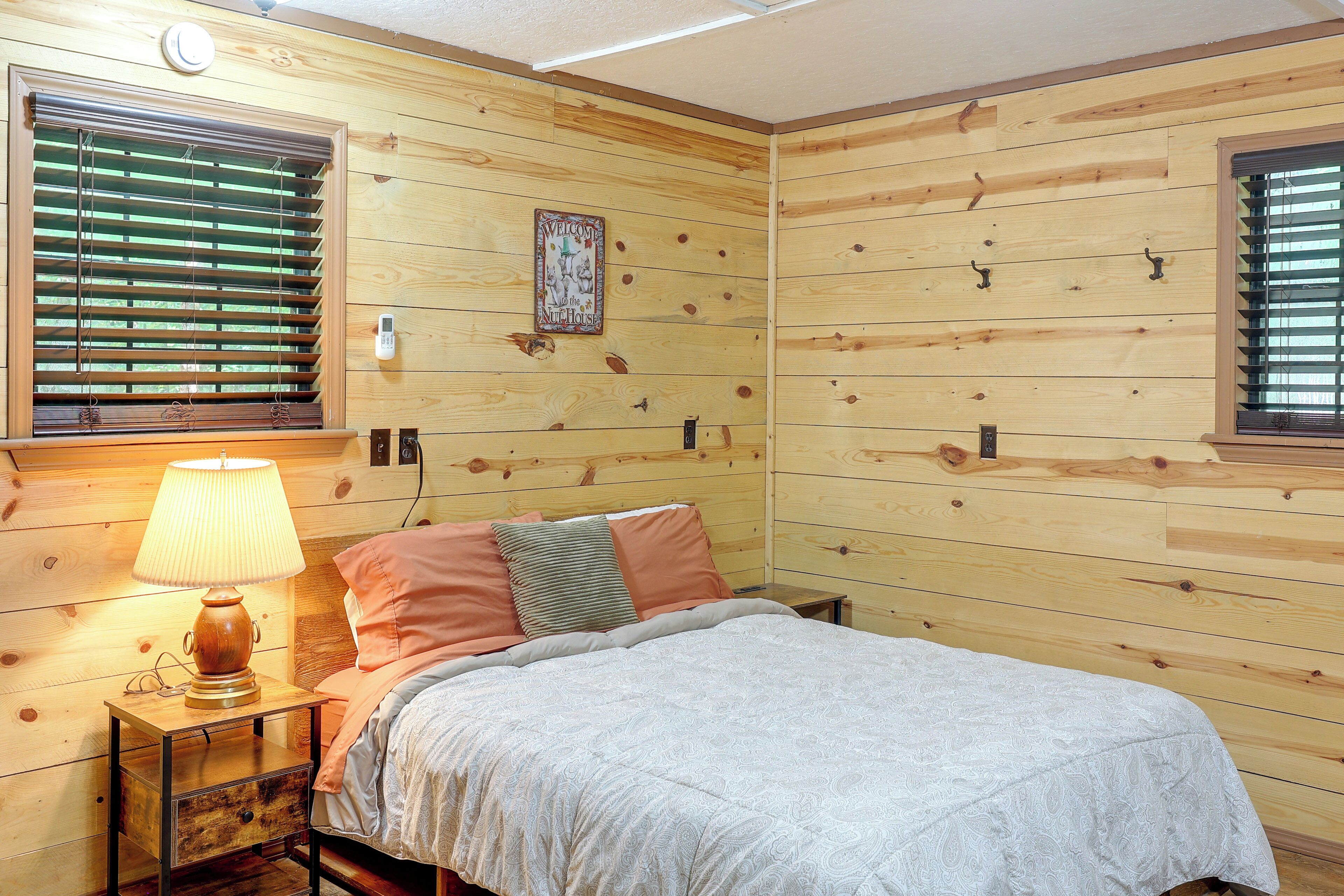 A wooden-paneled room with a bed, a nightstand, a lamp, and a wall-mounted thermostat.