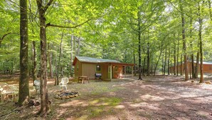 A rustic cabin with a porch, surrounded by a forest.