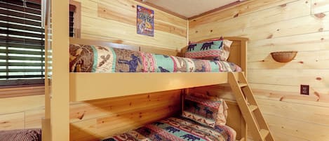 Una cama litera con escalera, paredes de madera y una ventana con persianas.