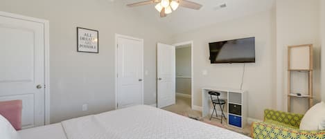 A bedroom with a bed, a ceiling fan, a TV, a desk, and a chair.