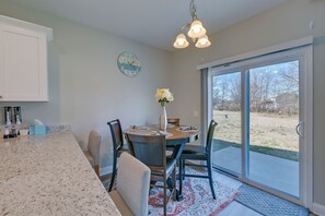 A kitchen with a granite countertop, a dining table with chairs, a vase with flowers, a clock on the wall, and a sliding glass door leading to a backyard. - Great for Groups! 2 Centrally Located Concord Gems (Concord)