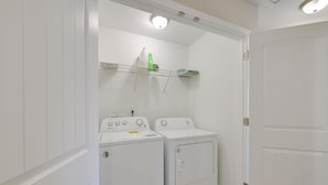 Un lavadero con dos lavadoras blancas y un estante encima.