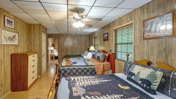 A room with two beds, wooden walls, a ceiling fan, and framed pictures.