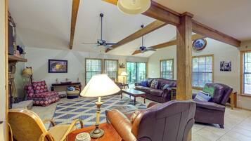 A spacious living room with high ceilings, exposed wooden beams, a fireplace, and large windows.