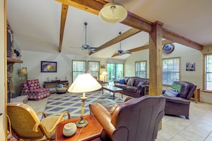 A spacious living room with high ceilings, exposed wooden beams, a fireplace, and large windows.