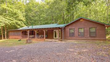 A wooden cabin with a porch, a covered outdoor seating area, and a gravel driveway.