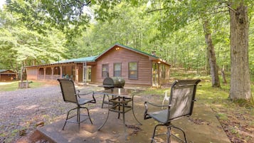 A cabin with a porch, a grill, and two chairs.