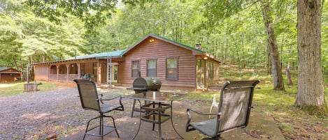 A cabin with a porch, a grill, and two chairs.
