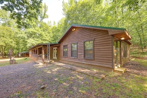 A cabin with a porch, a covered outdoor seating area, and a gravel driveway.