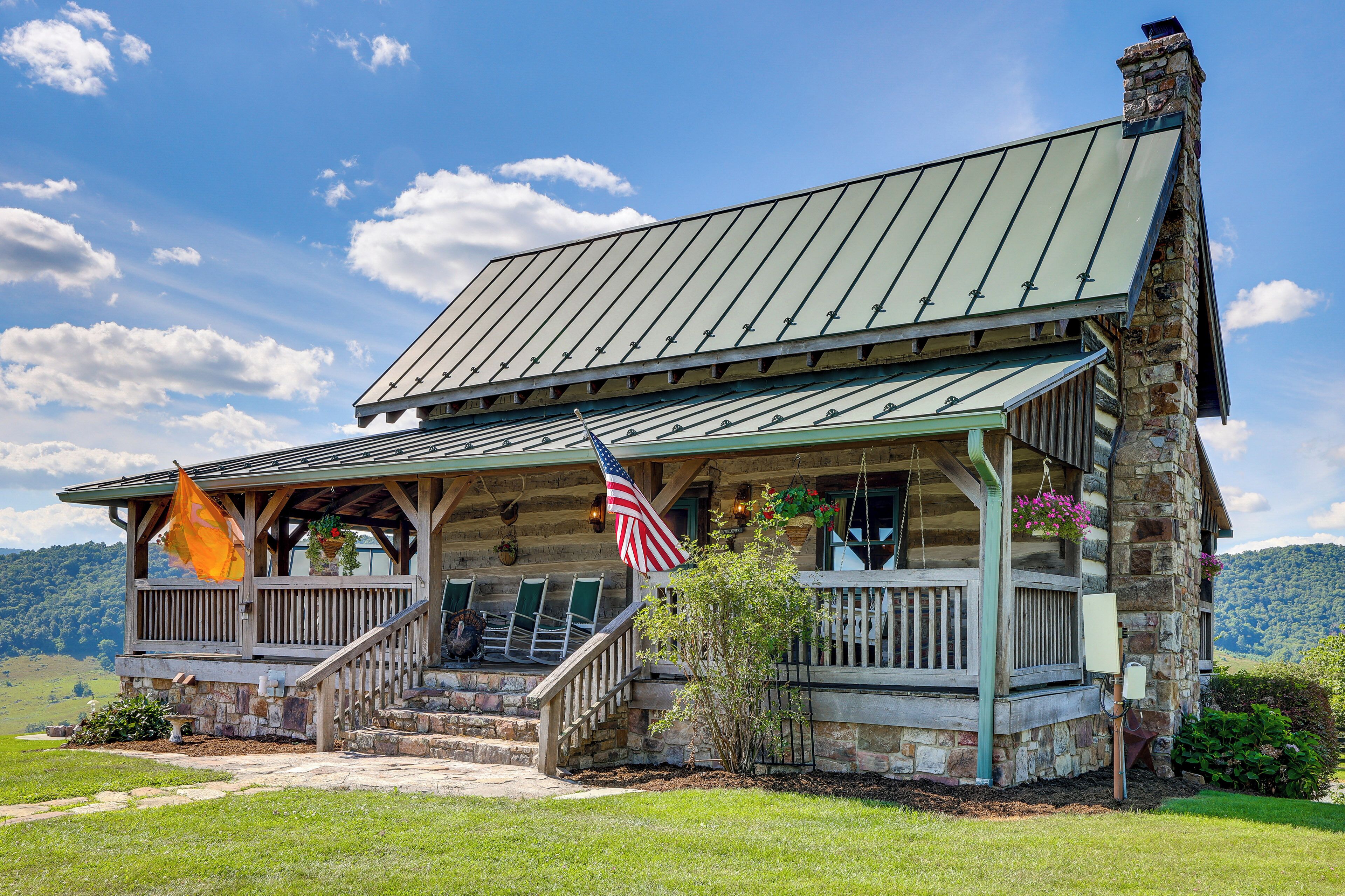 A rustic log cabin with a porch, stone foundation, and a flag.
