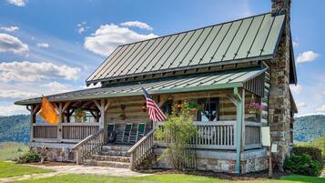 A rustic log cabin with a porch, stone foundation, and a flag.