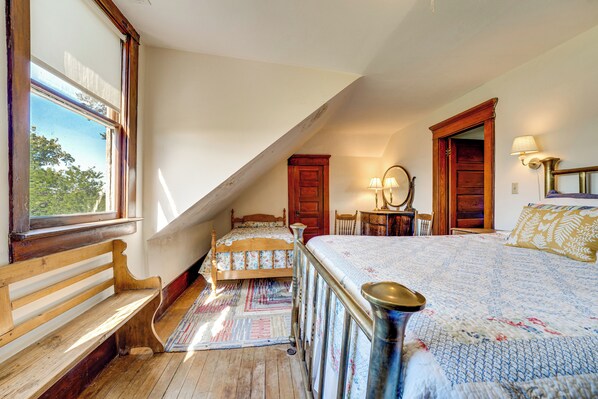 A bedroom with a sloped ceiling, wooden furniture, a bed with a floral bedspread, a bench, a small table, and a mirror.