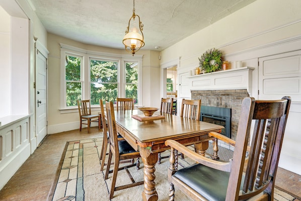 A dining room with a wooden table, chairs, a chandelier, and a fireplace.