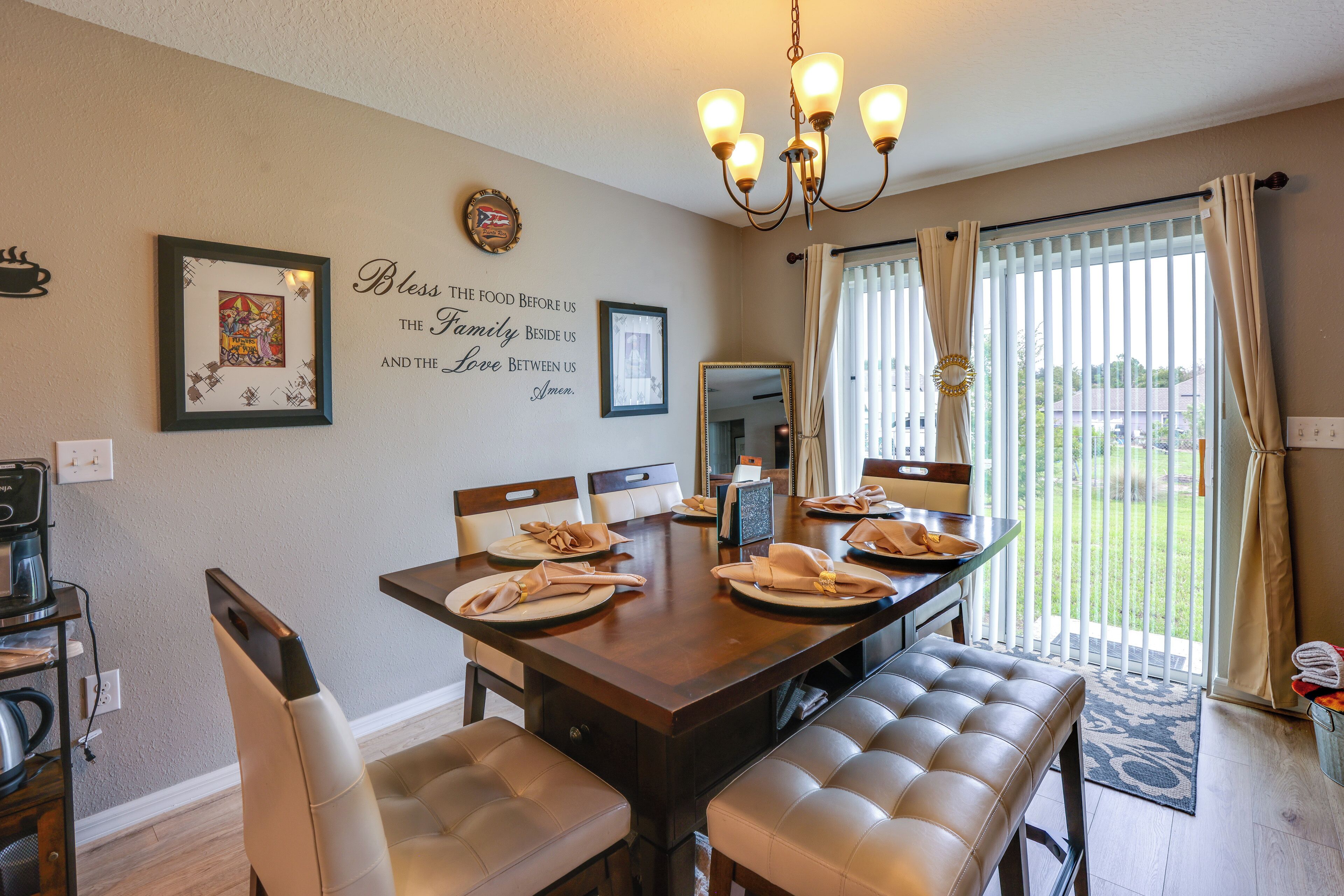 Un coin repas avec une table dressée pour quatre personnes, un lustre et un mur orné d’un message sur le thème de la famille.