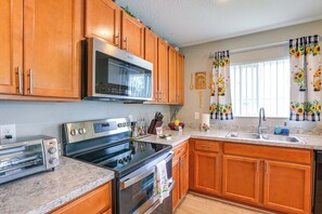 A kitchen with wooden cabinets, a microwave, a stove, a sink, and a window with sunflower curtains.