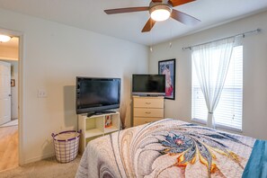 A bedroom with a bed, two TVs, a ceiling fan, a window with curtains, and a door. - Gateway to Disney! Home w/ Fenced Yard & Office (Mascotte)