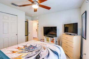 A bedroom with a bed, a TV, a dresser, and a ceiling fan.