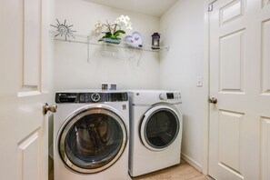 A laundry area with two front-loading washing machines, a shelf with decorative items, and a door. - Gateway to Disney! Home w/ Fenced Yard & Office (Mascotte)