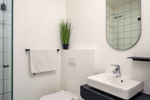 A bathroom with a white sink, a mirror, a towel rack, and a potted plant. - The Urban Nest by CTHA (Cape Town)