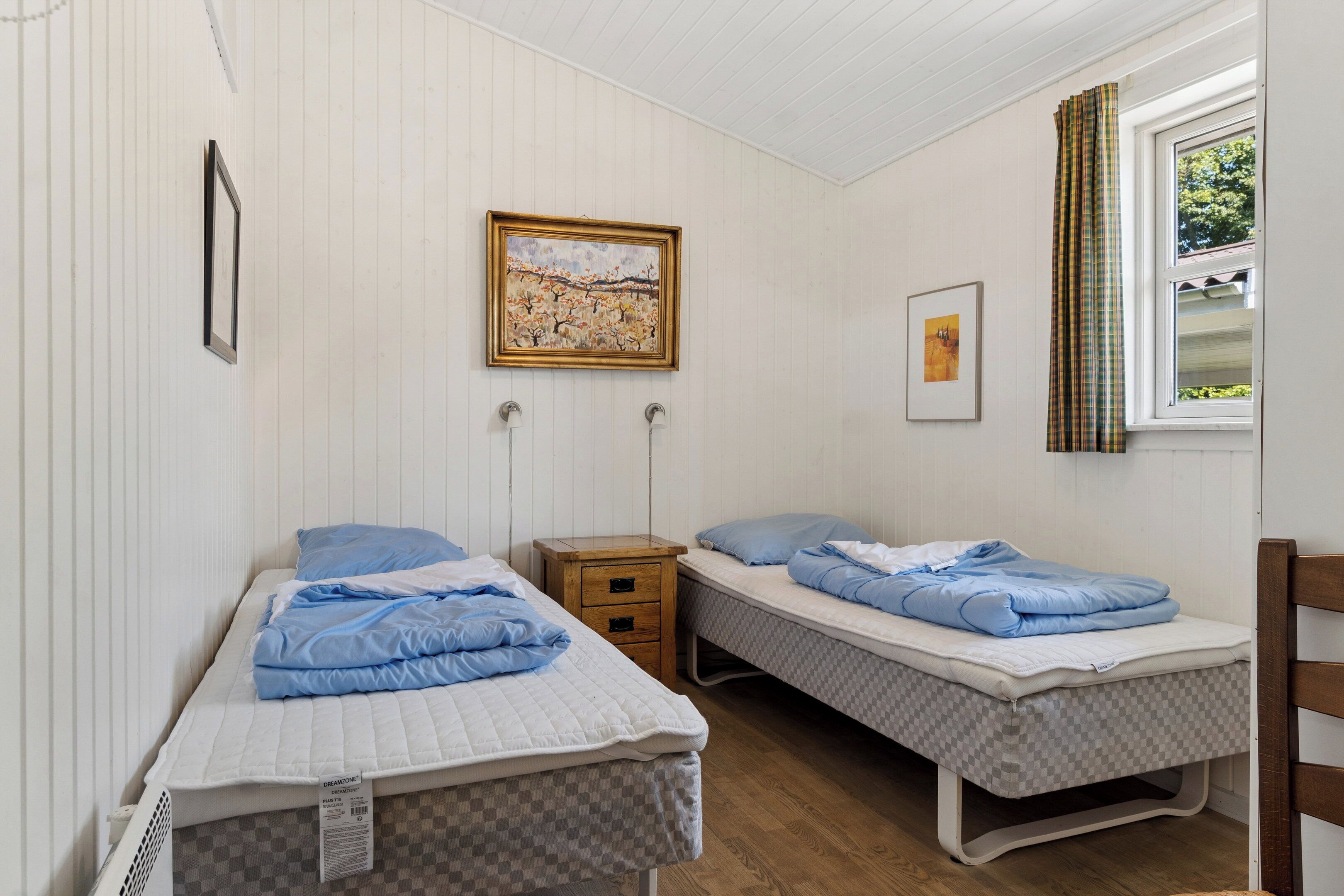 A room with two single beds, a wooden nightstand, a small table, and a window with curtains.