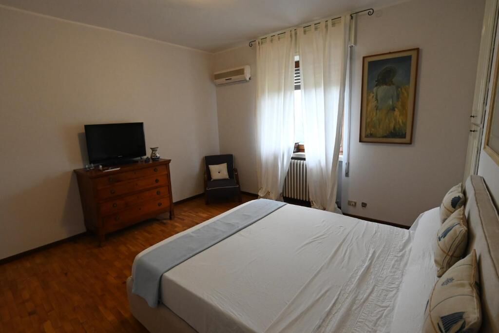 Ein Schlafzimmer mit einem Bett, einem Schminktisch, einem Fernseher, einem Sessel, einer Heizung und einem Bild an der Wand.
