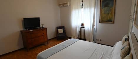 A bedroom with a bed, a dresser, a television, a chair, a radiator, and a painting on the wall.