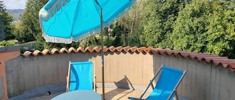 A rooftop terrace with a round table, two blue lounge chairs, and a large blue umbrella.