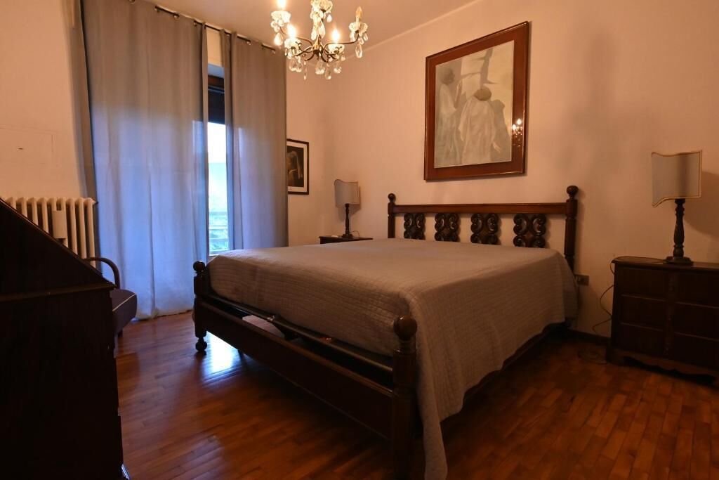 A bedroom with a wooden bed, a chandelier, a framed artwork on the wall, and a radiator.