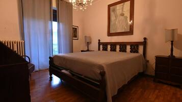 A bedroom with a wooden bed, a chandelier, a framed artwork on the wall, and a radiator.