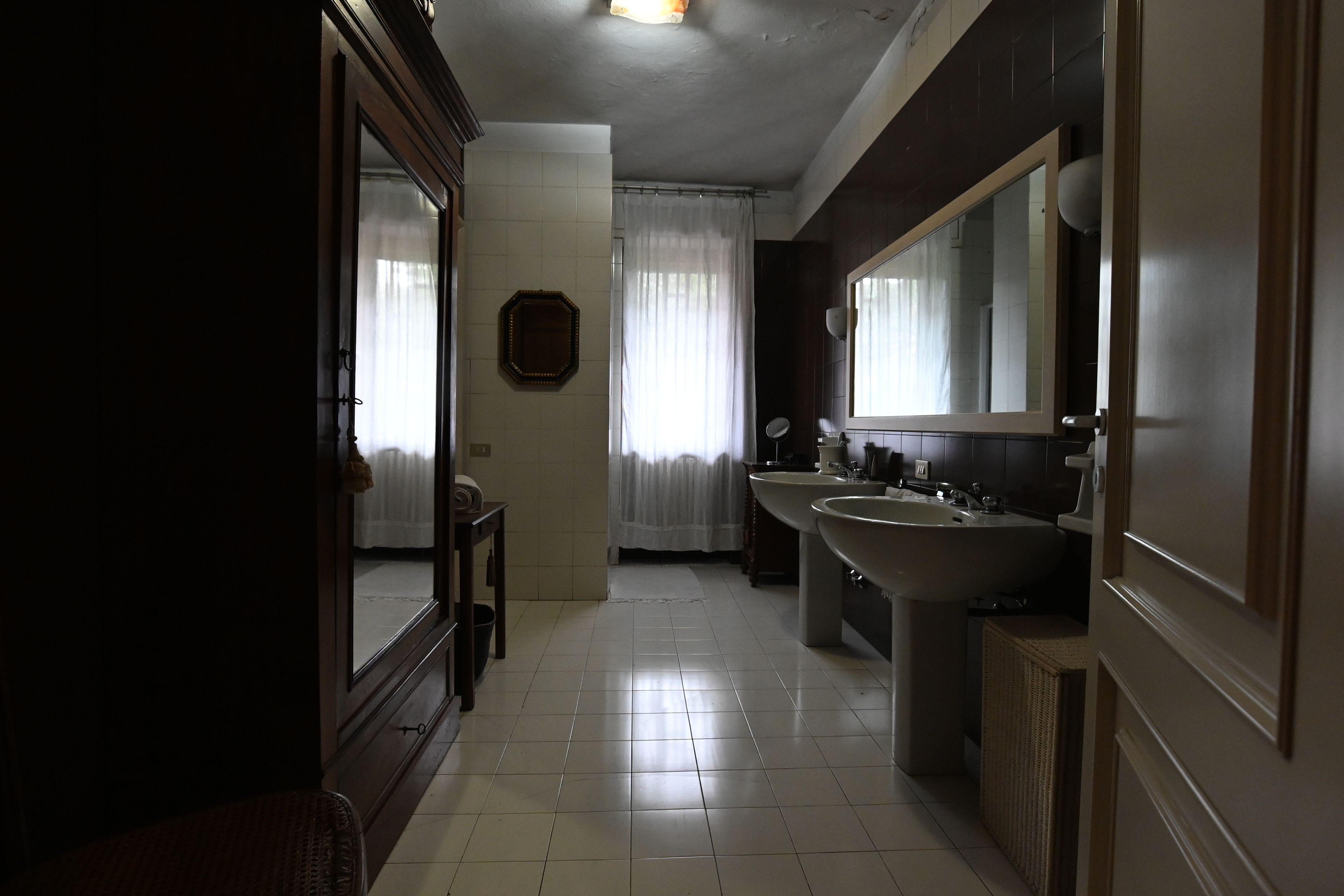 A bathroom with a large mirror, two sinks, and a window with curtains.