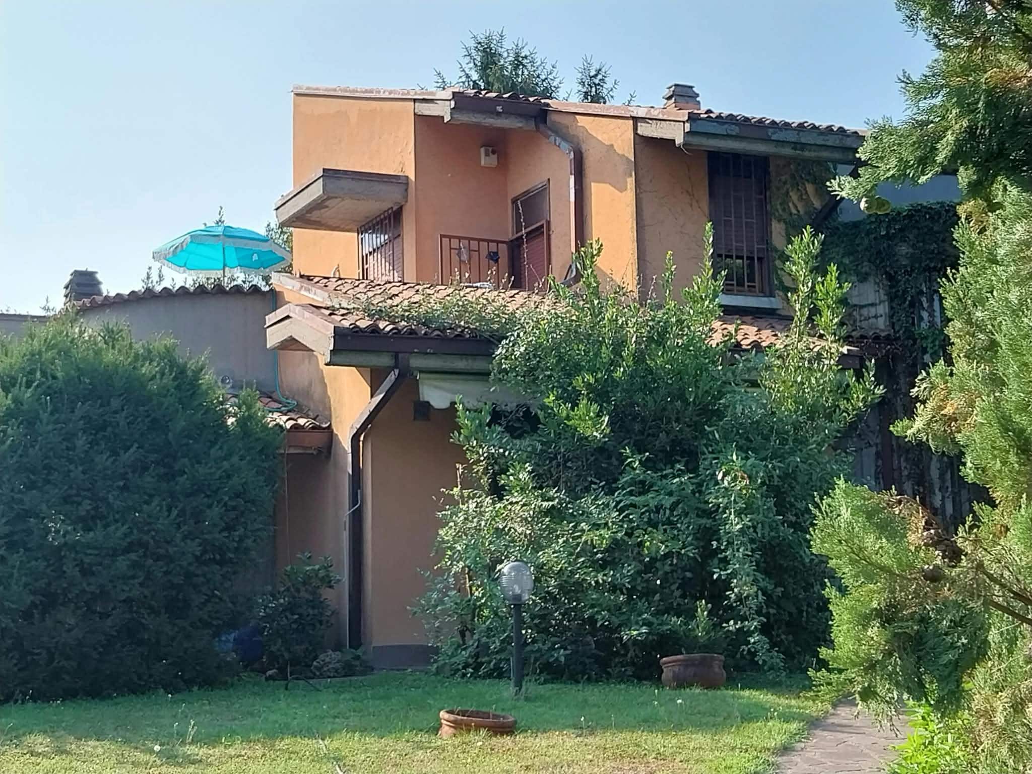 A two-story building with a balcony, surrounded by greenery and a clear sky.